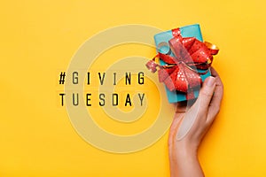 Giving Tuesday. Global day of charitable giving after Black Friday shopping day. Woman hand holding gift box on yellow background