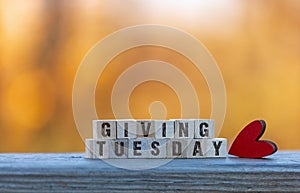 Giving Tuesday text on wood blocks with red heart golden leaves bokeh background