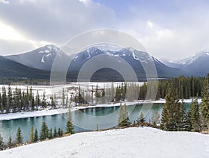 Glacial turquoise river in foreground of snow covered landscape and majestic mountain range.