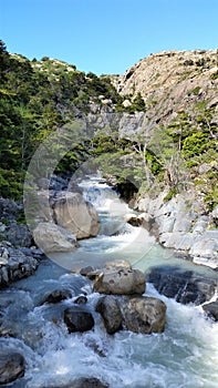 Glacier-fed stream with boulders on the W Trek in Torres del Paine green hills in Patagonia, Chile