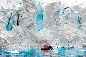 Glacier ice shelf wall in Antarctica, people in Zodiac in front of edge of glacier