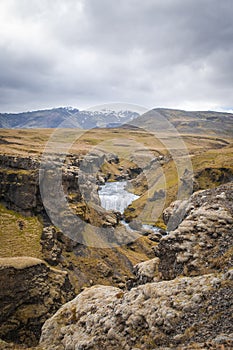 Glacier river flowing downhill in a valley between volcanic land