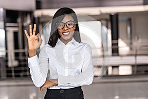 Glad african office worker with light-brown skin showing okay sign after conference. Portrait of female black freelancer enjoying