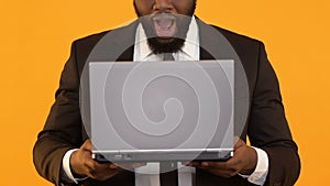 Glad Afro-American man holding laptop and making wow gesture, business e-mail