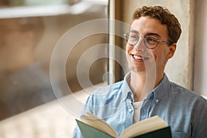 Glad calm handsome european young man student in glasses read book, enjoy peace