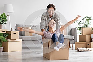 Glad caucasian young man pushes wife in cardboard box have fun in living room interior