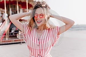 Glad charming woman playing with her hair while posing in amusement park. Outdoor photo of amazing