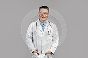 Glad confident attractive adult japanese doctor in white coat, glasses with stethoscope look at camera