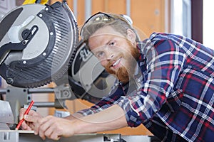 Glad diligent man wearing protective workwear operating circular saw