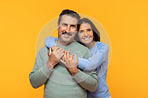 Glad european old woman embraces man from behind with a joyful expression, both smiling