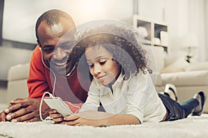 Glad father and kid using mobile phone with earpieces