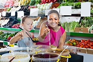 Glad female with daughter taking pickled olives