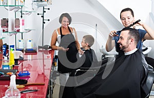 Glad female hairdresser cutting male client