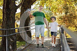 Glad little mixed race kid and old caucasian grandfather enjoy free time, have fun together, playing with airplane