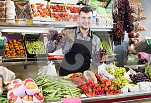 Glad male seller showing assortment of grocery shop photo