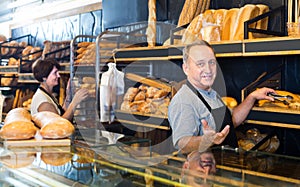 glad mature bakers with fresh bread in bakery