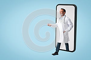 Glad old male doctor in white coat with stethoscope comes out of phone, greets with hand