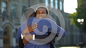 Glad parent hugging young son in suit outdoors university, prom celebration photo