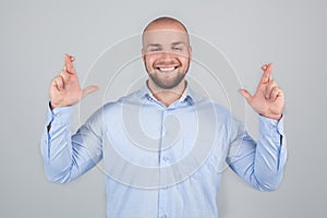 Glad positive bearded man crosses fingers, closes eyes with pleasure, anticipate hearing good news,  white background.