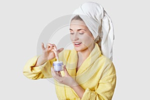 Glad relaxed young Caucasian woman with fresh healthy skin, going to apply cream on skin, has beauty treatments after shower,