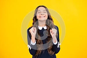 Glad teenager girl crosses fingers, closes eyes with pleasure, anticipate hearing good news, isolated yellow background
