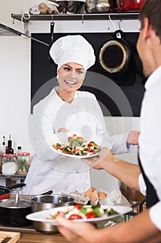 Glad woman cook giving salad to waitress