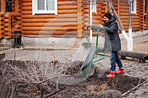 Glad woman in field clothes applying mulching procedure, pouring old dried leaves, bark. Pouring grass and muck soil