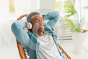 Glad young african american man with closed eyes in headphones enjoys favorite music and peace