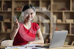 Glad young asian woman with down syndrome in headphones with laptop point finger at camera in office