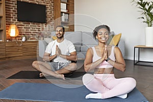 Glad young black couple in sportswear doing exercises, practicing yoga on mat, enjoy comfort, calm and silence