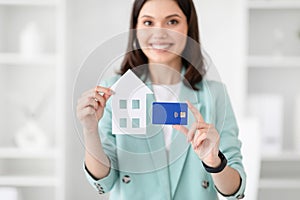 Glad young caucasian businesswoman in suit hold credit card and house