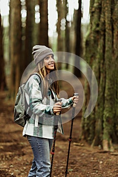 Glad young caucasian lady tourist in jacket with trekking sticks walk in forest alone, enjoy trip
