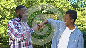 Glad young father and son fist bumping outdoors, family generations, having fun