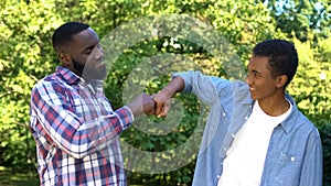 Glad young father and son fist bumping outdoors, family generations, having fun