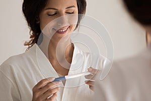 Glad young latin woman stand by mirror hold pregnancy test