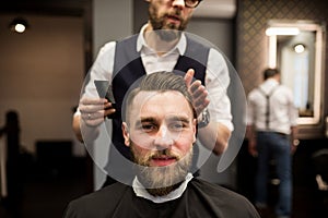 Glad young man having hair cut at barber salon