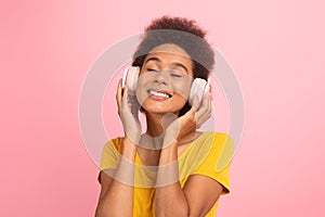 Glad young mixed race woman with curly hair in wireless headphones with closed eyes enjoys favorite music