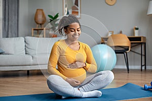 Glad young pregnant african american woman touching big belly and enjoying baby move, practicing yoga