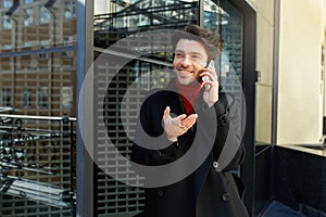 Glad young pretty brown haired man with trendy haircut raising emotionally palm while havingphone conversation and smiling happily