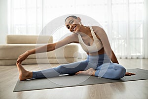 Glad young slim latin woman in sportswear doing hand, legs stretching on mat
