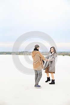 Gladden man and woman going on snow and holding hands, wearing coats and scarfs.