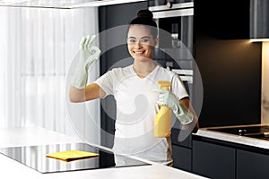 Gladful female doing the housework while using a spray in the kitchen. Young woman showing ok gesture.