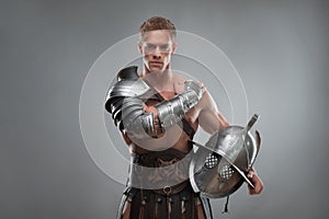 Gladiator in armour posing with helmet over grey