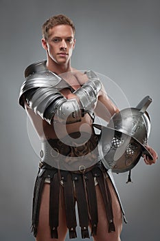 Gladiator in armour posing with helmet over grey