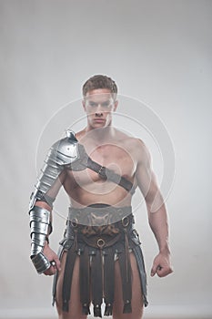 Gladiator in armour posing over grey background