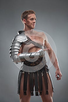 Gladiator in armour posing over grey background