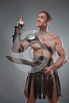 Gladiator in armour posing with sword over grey