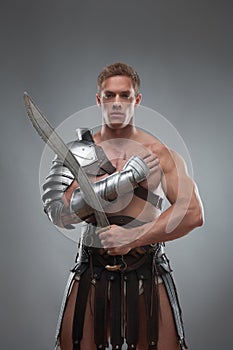 Gladiator in armour posing with sword over grey