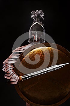 Gladiator with sword and armor on a black background. A warrior in gladiatorial armor and a helmet hides behind a shield