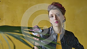 Glamorous aggressive lady in punk rock style party clothes with dark pink hair in black leather jacket and long earrings